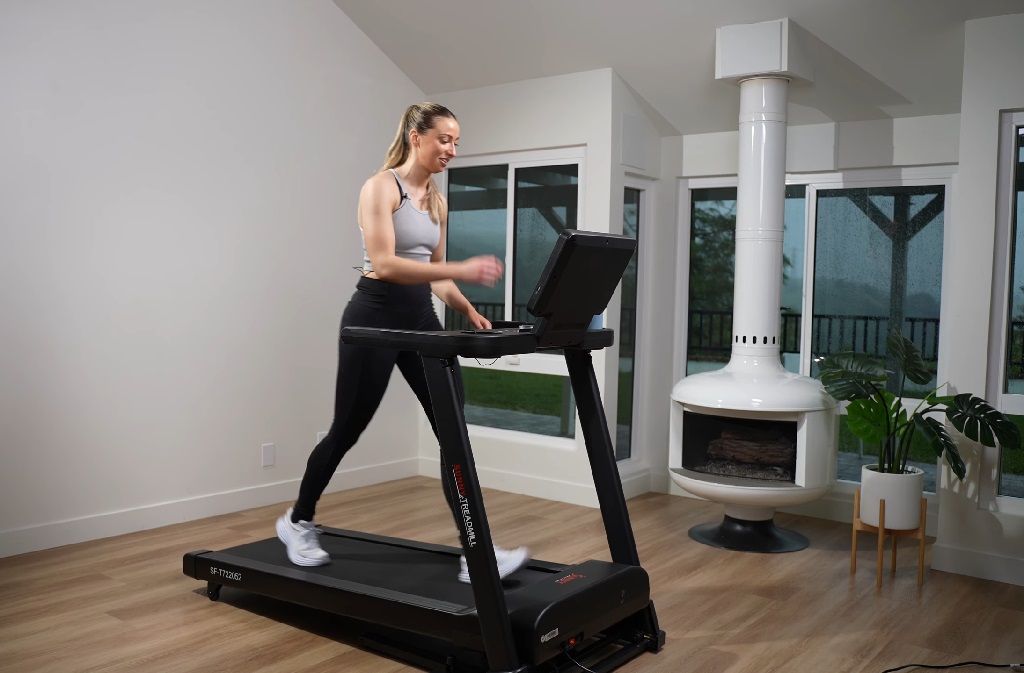 A woman using an incline treadmill in a brightly lit living room with modern decor