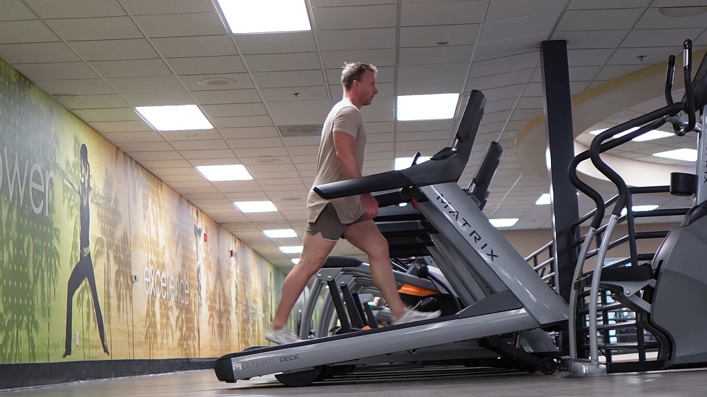 A man walking on an incline treadmill at a gym surrounded by workout equipment