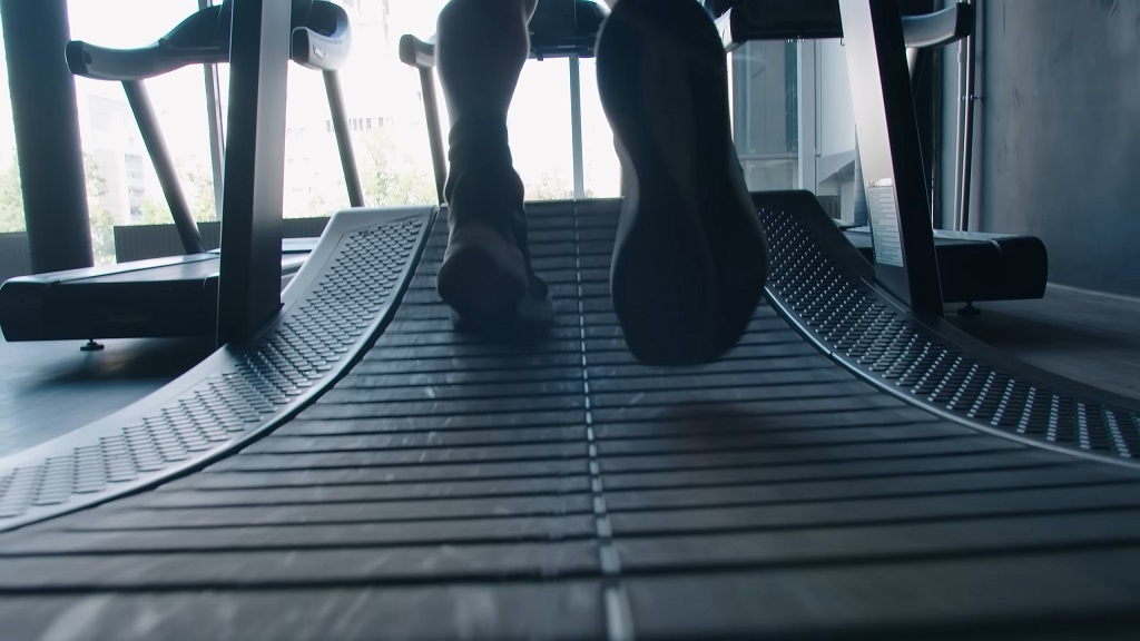 Close-up of a person's feet running on a treadmill set at an incline in a fitness center